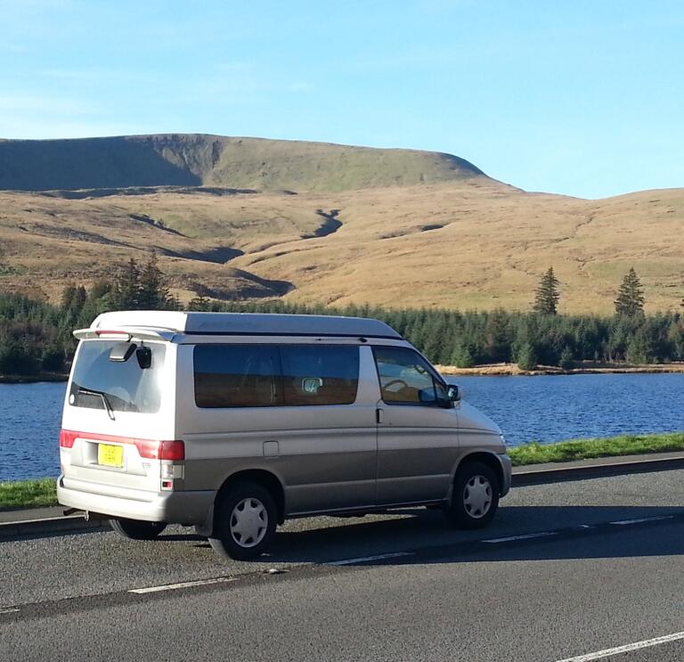 campervan on route with view of reservoir and mountain.