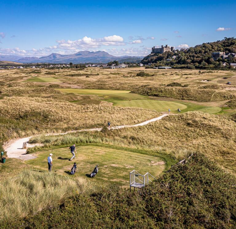 People playing on a coastal golf course with a castle in the distance. 