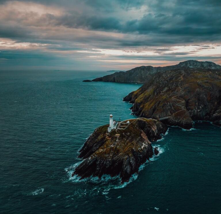 A lighthouse on a rocky peninsula against a dark blue sea and sky
