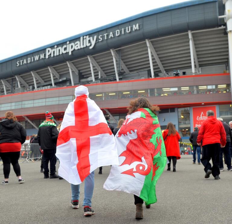 man wearing England flag and woman wearing Welsh flag walk towards Principality Stadium, Cardiff.