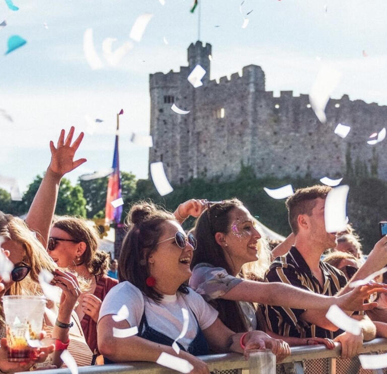 Audience at a music gig in Tafwyl standing behind a barrier with confetti in the foreground and Cardiff Castle in the background.