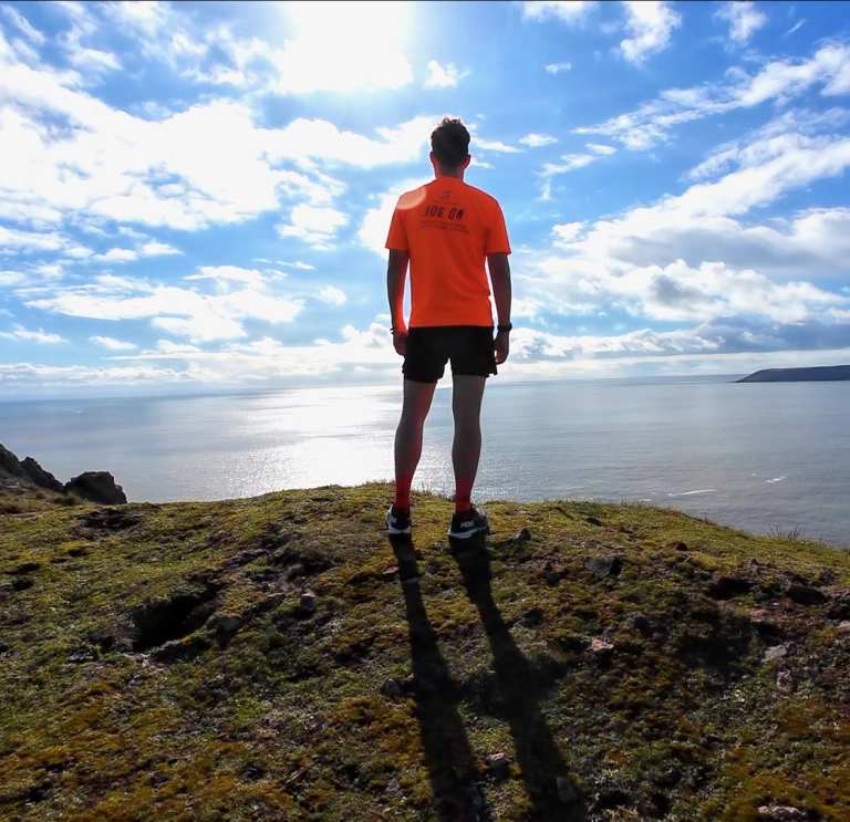A man in tshirt and shorts looking over a wide sandy beach, under blue skies.