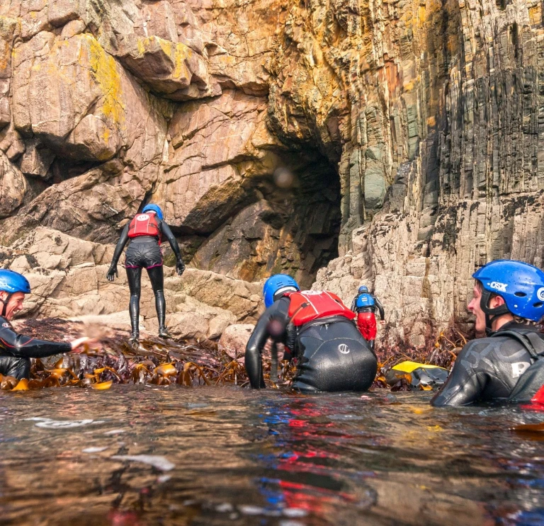 Grŵp o bobl yn gwisgo offer diogelwch dŵr yn y dŵr ger yr arfordir