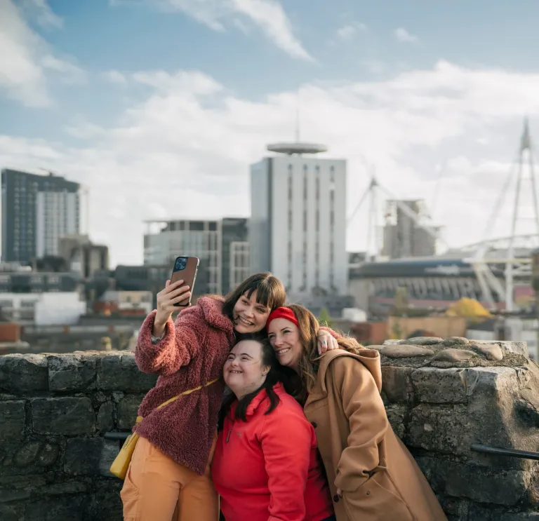 Two women and girl taking selfie on top of castle with view of modern buildings.