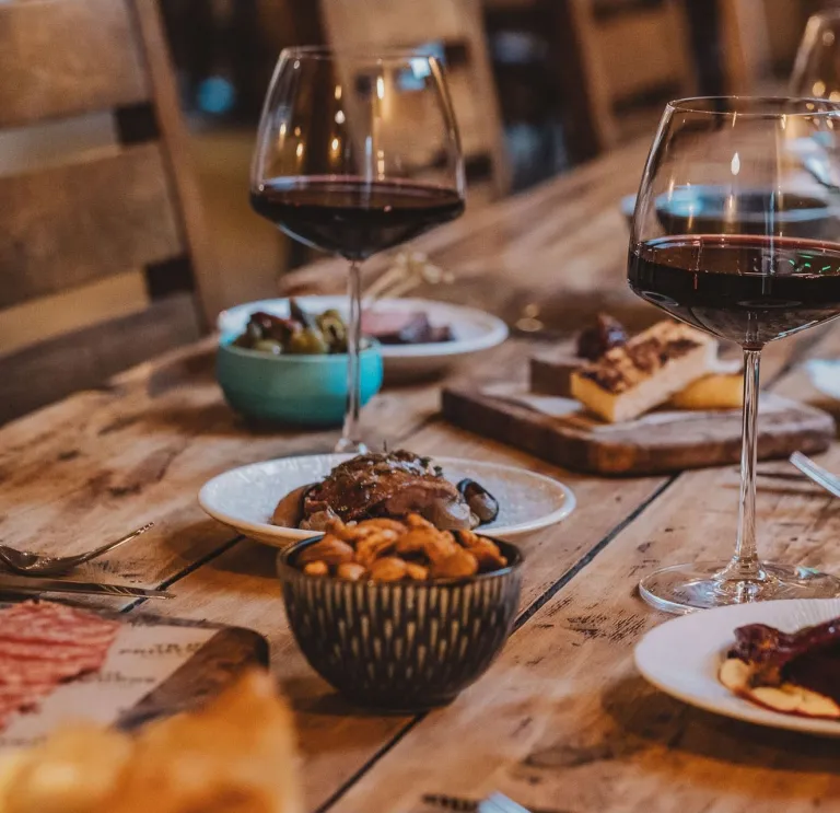 wooden table with tapas dishes and glasses of red wine.