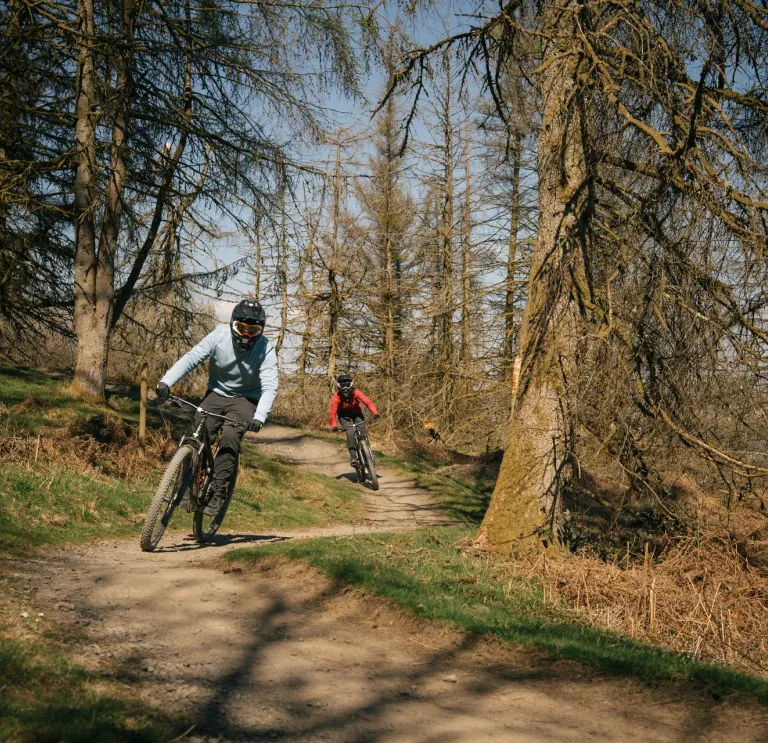 Two people mountain bikes on trail in bike park.