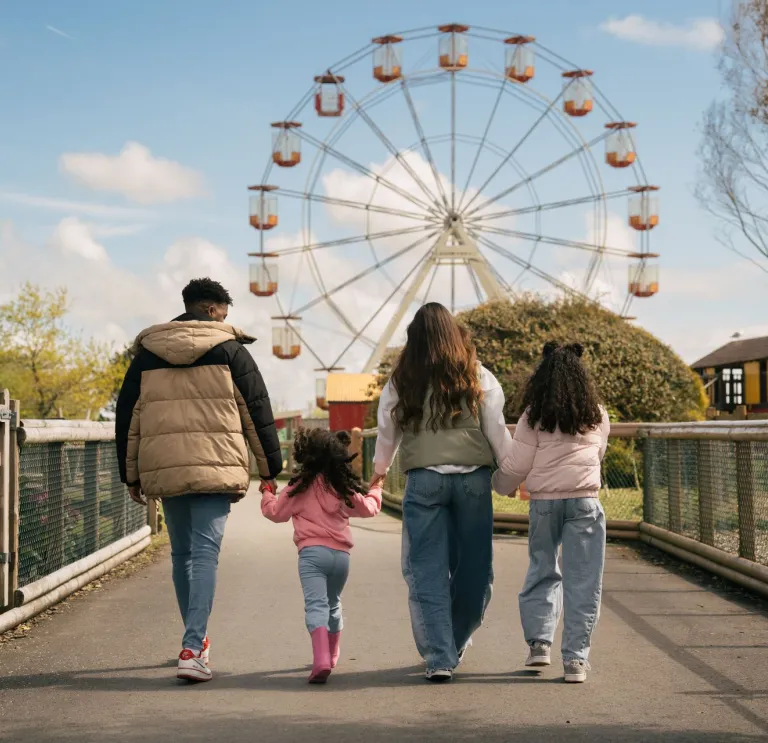 Two adults and two children walking towards a ferris wheel.