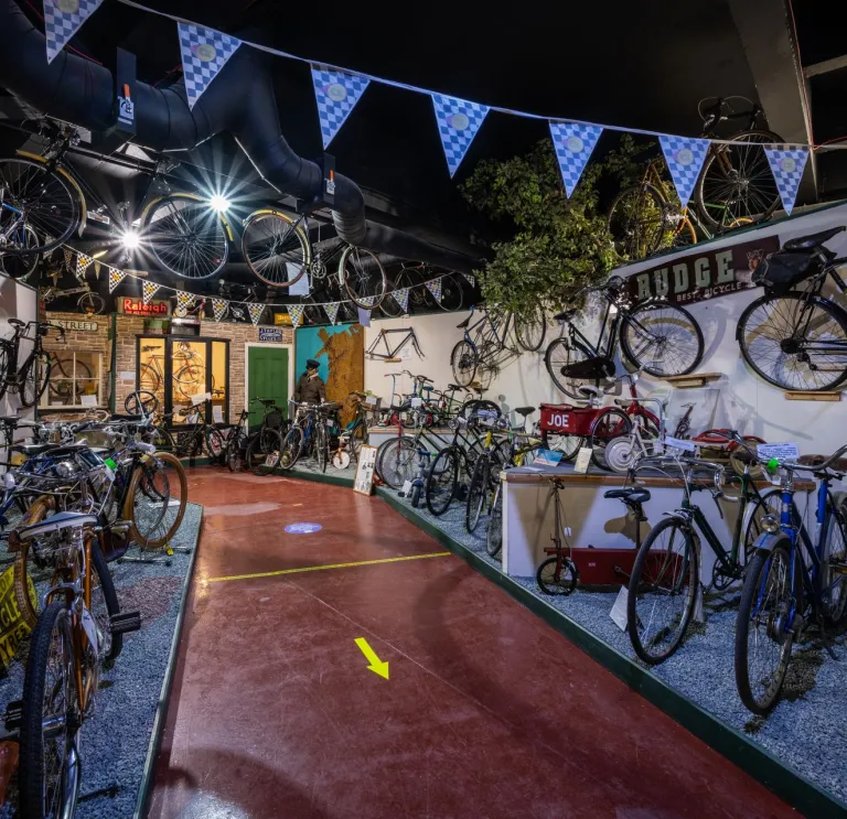 A museum full of bicycles all over the place, on the walls, on floor level displays.