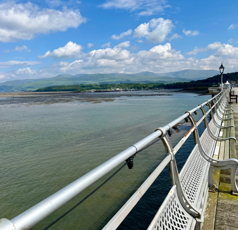 Looking down a long Victorian style pier with the headland and sea in the distance.