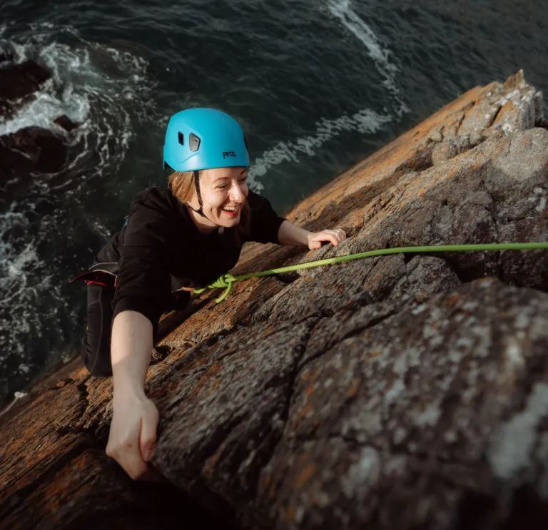 smiling climber wearing helmet climbing sea cliff.