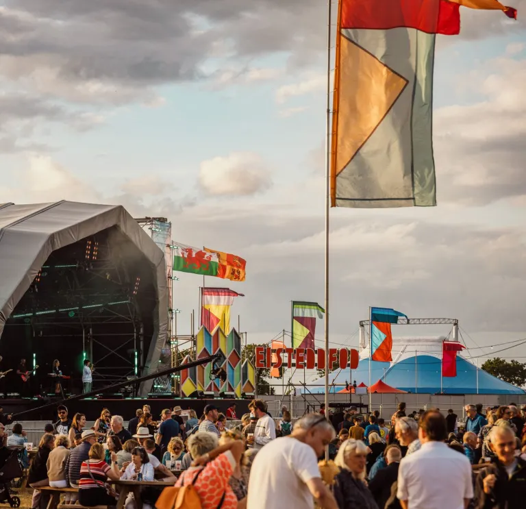 crowd enjoying Eisteddfod with stage and flags.