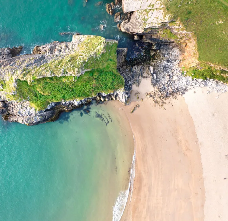 A golden sand beach with a rocky outcrop jutting into a  turquoise sea. 