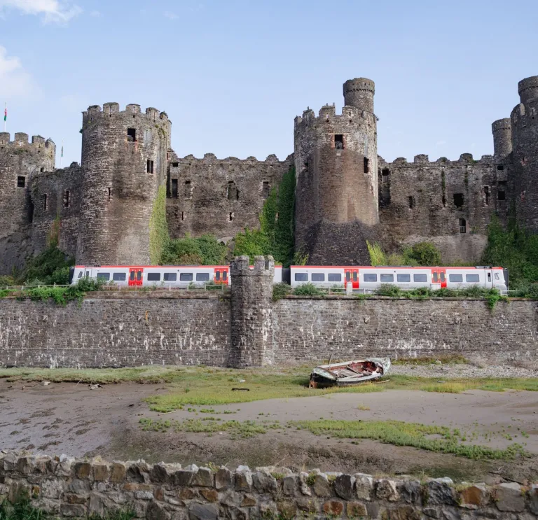 A train travelling alongside a large stone castle.