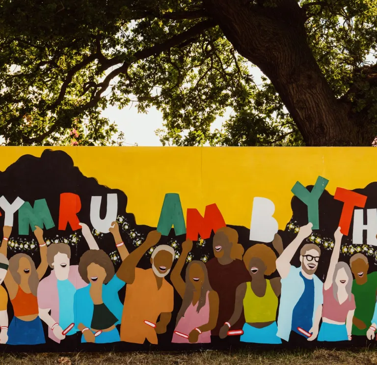 A colourful mural with loads of people holding up 'Cymru am byth' letters.