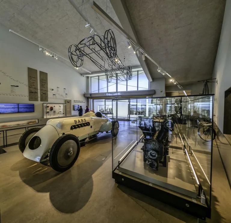 Interior of the Museum of Land Speed in Pendine, showing the historic 'Babs' racing car and engine displays in a bright gallery.