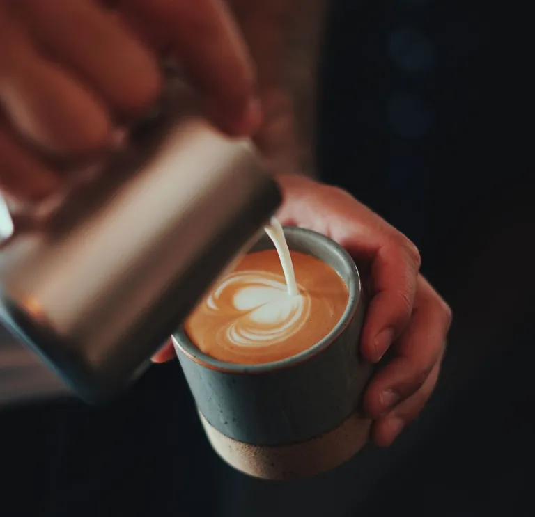 Barista pouring milk into a cup of coffee