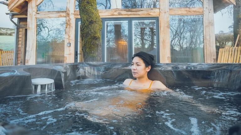 Woman relaxes in a hot tub outside a luxury treehouse.