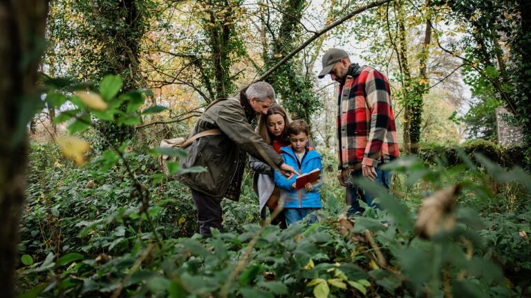 A family with a young boy In the woodswith a forager guide showing them a guide book