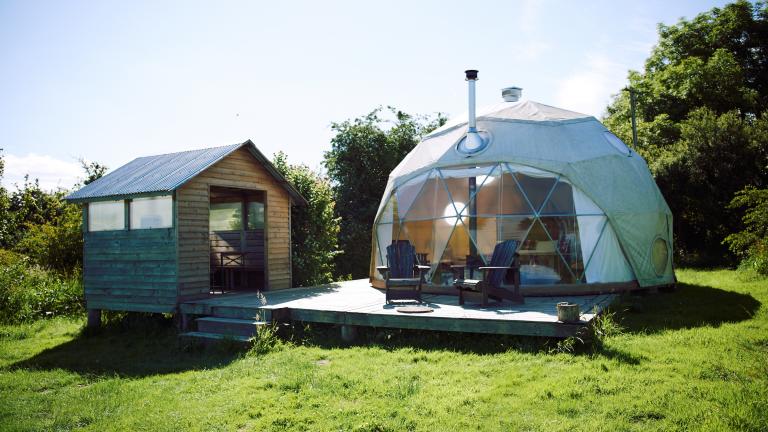  Image of a dome tent and a small hut in a field.