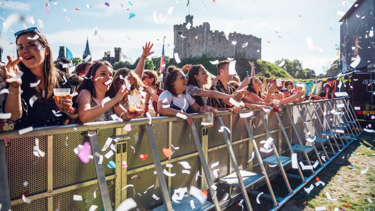 Audience at a music gig in Tafwyl standing behind a barrier with confetti in the foreground and Cardiff Castle in the background