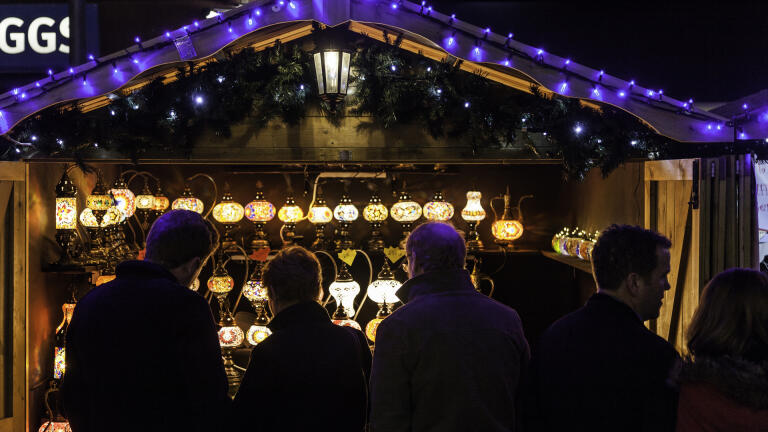 nighttime shot of Christmas market stall selling lamps with people in the foreground.