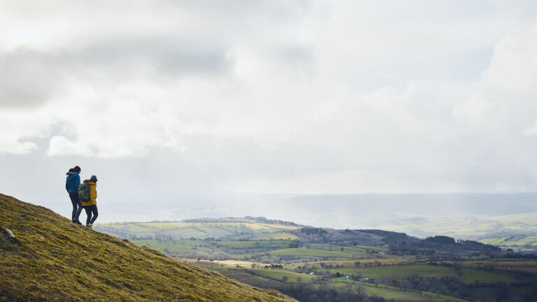 Two walkers on Hay Bluff looking out over countryside.