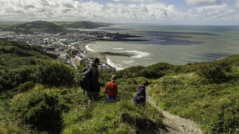 man and two children walking with view towards Aberystwyth coast.