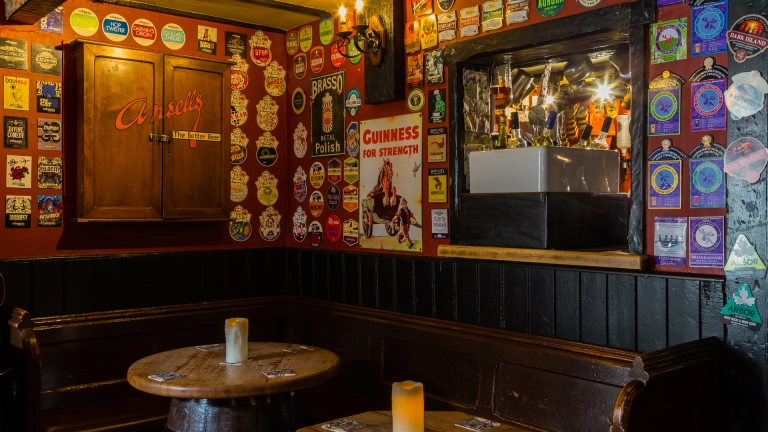 Innenraum eines alten Gasthauses mit Bierdeckeln an den Wänden und Tischen aus alten Fässern..