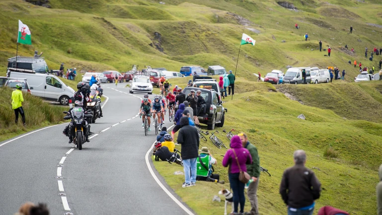 Radfahrer und Zuschauer an einer Straße in einer grünen hügeligen Landschaft