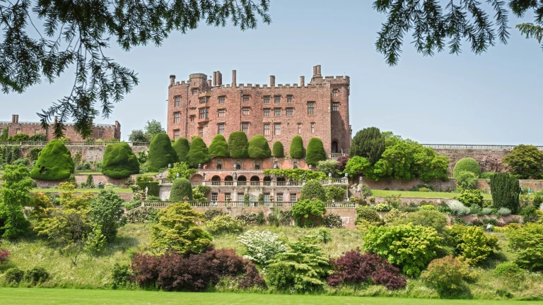 Gardens in front with Powis Castle on the horizon against blue sky.