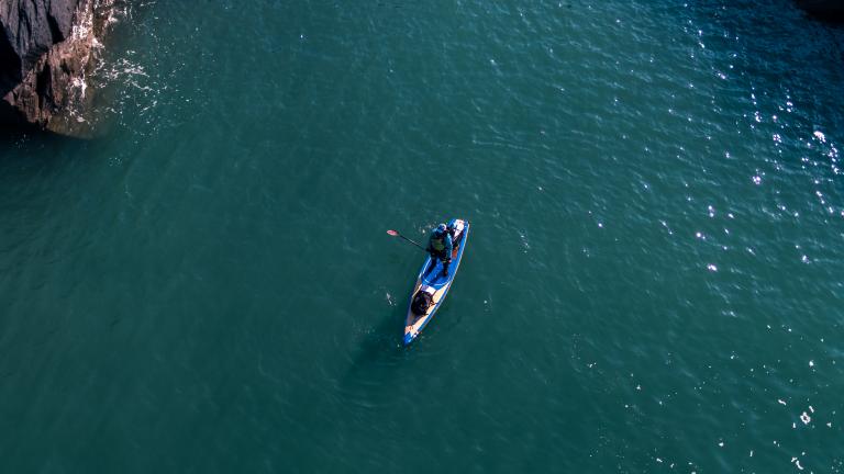 Paddleboarder on a deep blue sea from above.