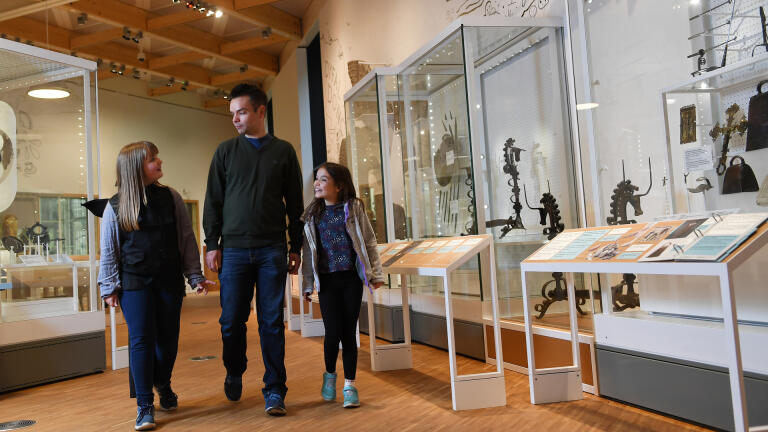 Eine dreiköpfige Familie beim Betrachten von Museumsvitrinen.