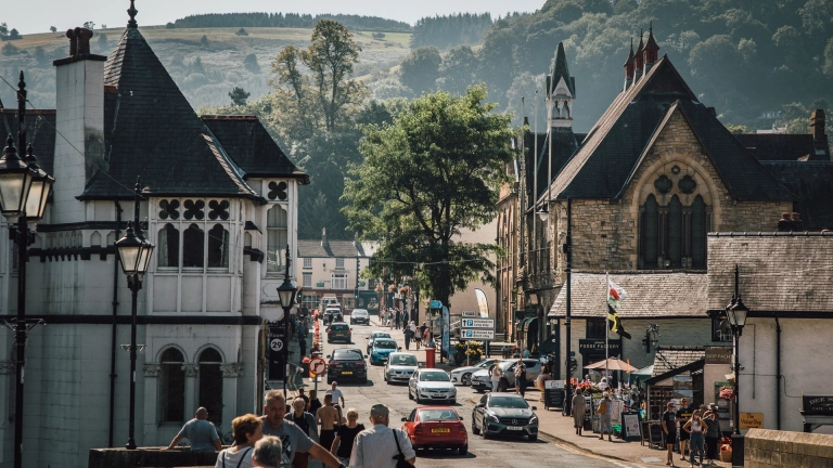 Stadt mit vielen Spaziergängern und Autos sowie Landschaft im Hintergrund.