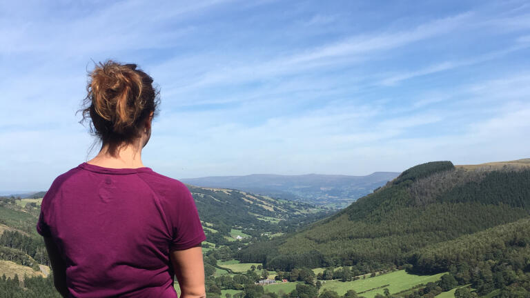A woman in a purple walking top looking down onto a green valley.