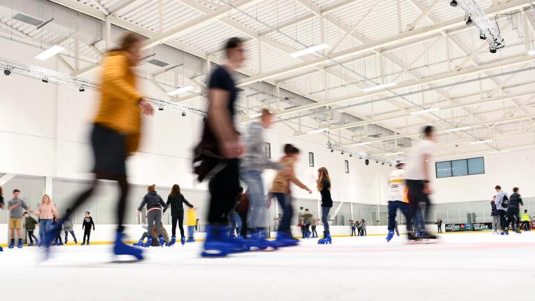 Indoor skating rink with people skating blurred action.
