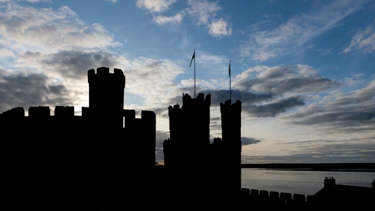 Silhouette of castle turrets and walls against a cloudy blue sky.
