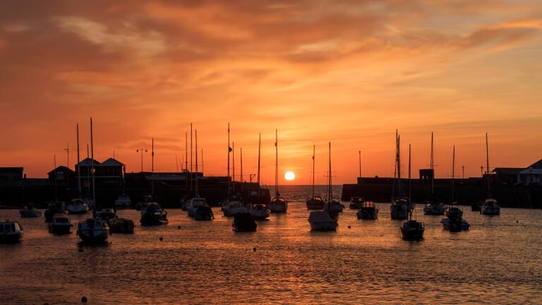 Sunset over a harbour with silhouettes of sailing boat masts.