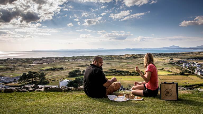 Two people having a picnic overlooking a coastal golf course.