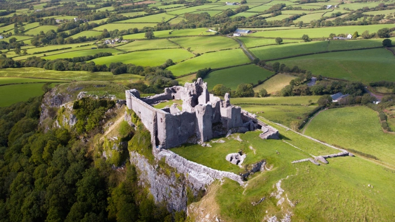  Luftaufnahme einer Burg auf einem Hügel inmitten grüner Felder.