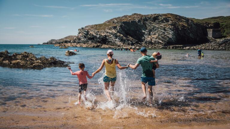 Two adults, and two children running into the sea on a sandy beach on a sunny day.
