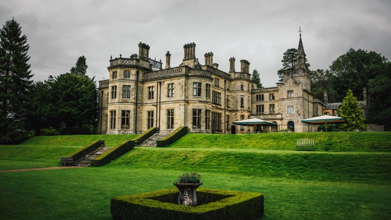 Ein kunstvoll verziertes viktorianisches Herrenhaus aus hellem Stein, umgeben von gepflegten Rasenflächen.
