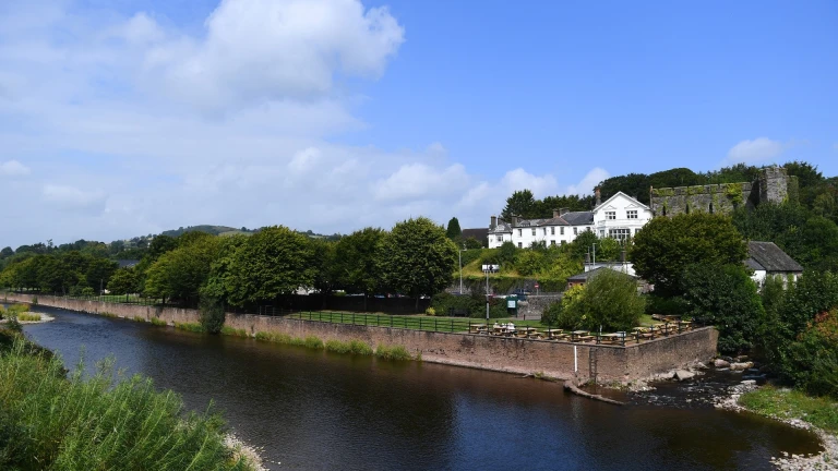 A large white hotel and castle overlooking a river, with a promenade alongside.