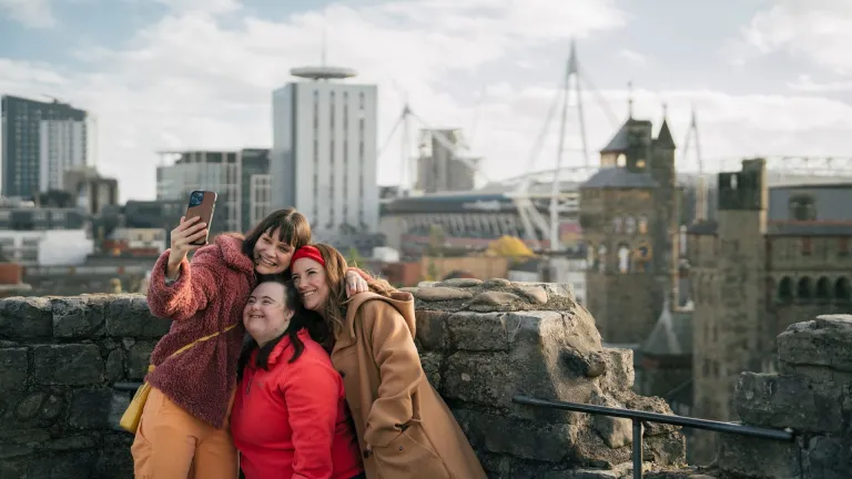 Two women and girl taking selfie on top of castle with view of modern buildings.