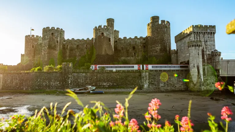 A train travelling alongside a large stone castle.