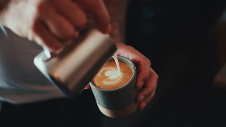 Barista pouring milk into a cup of coffee