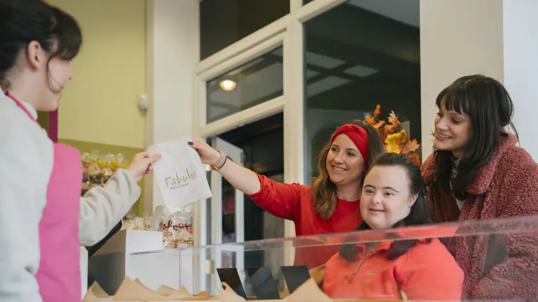 Customers collecting a bag of Welshcakes at a bakery counter while staff serve behind the display.