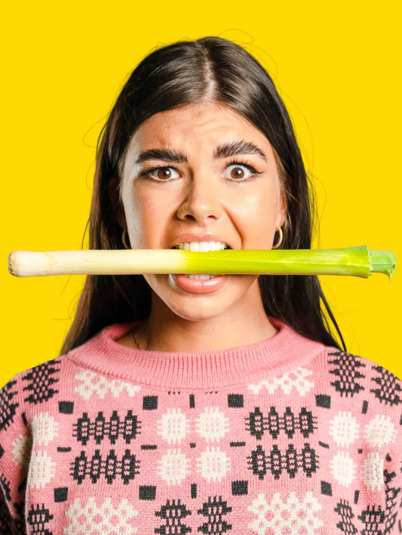 Woman wearing holding a leek between her teeth