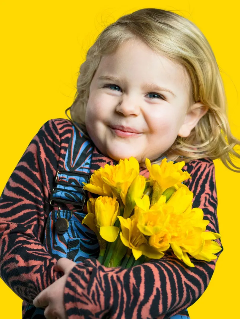 child smiling and holding a bunch of yellow daffodils