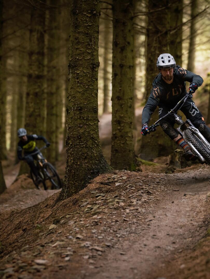 Mountain bikers riding on a trail through woodlands.