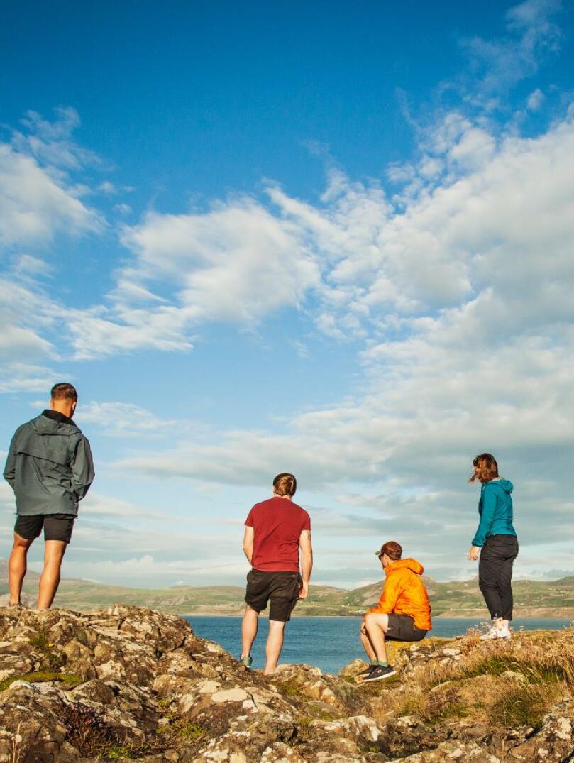 Group of people standing on rocks on the Wales Coast Path looking out to sea.